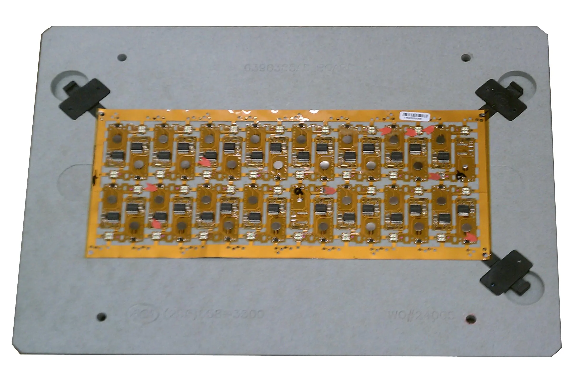 Flex PCB in a custom assembly fixture with visible tooling holes for alignment.