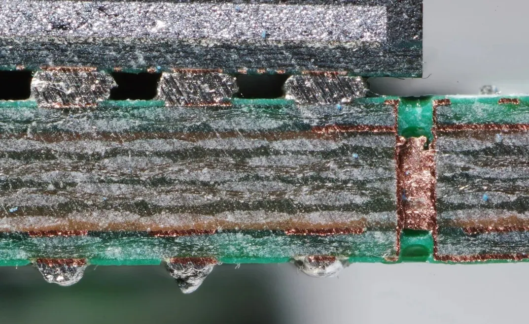 PCB cross-section under microscope revealing internal layers and vias.