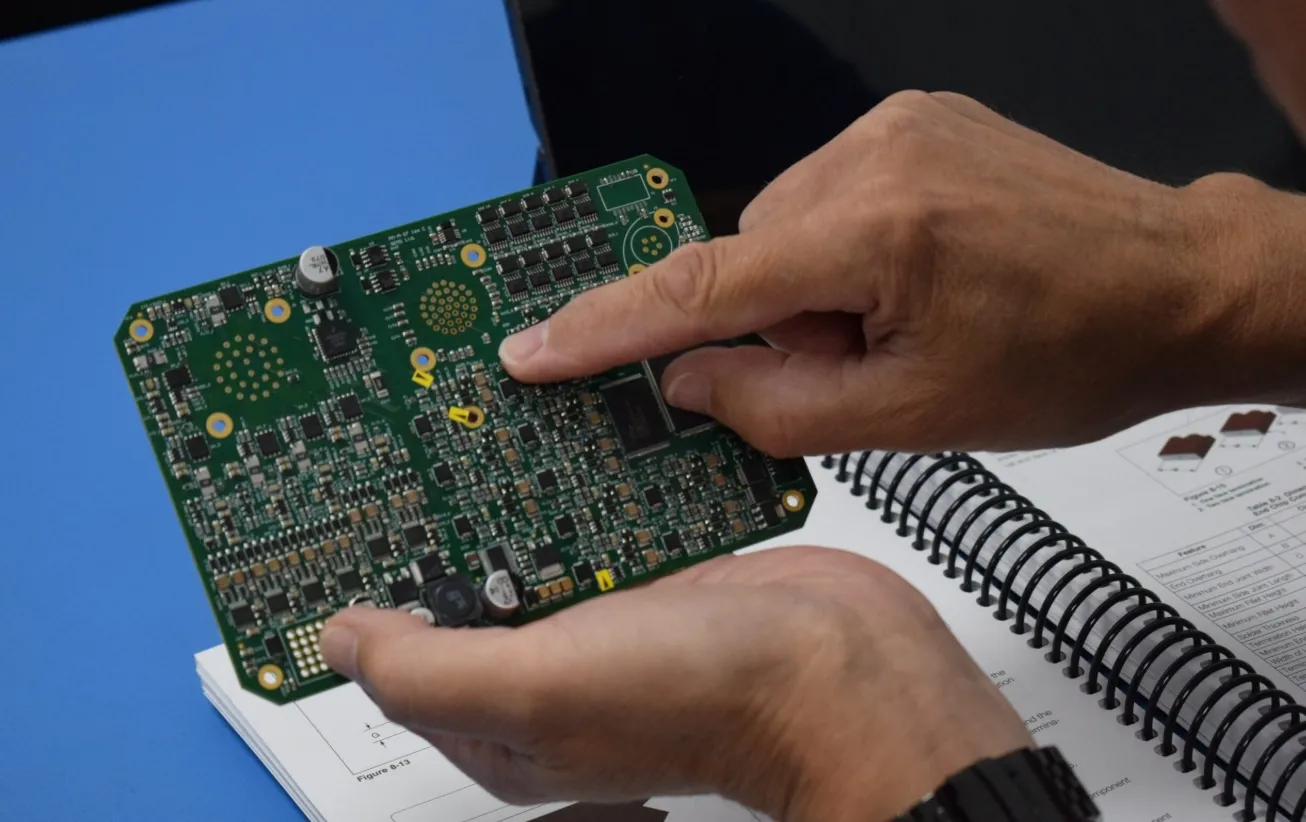 Technician performing PCB assembly inspection under IPC-A-610 guidelines.
